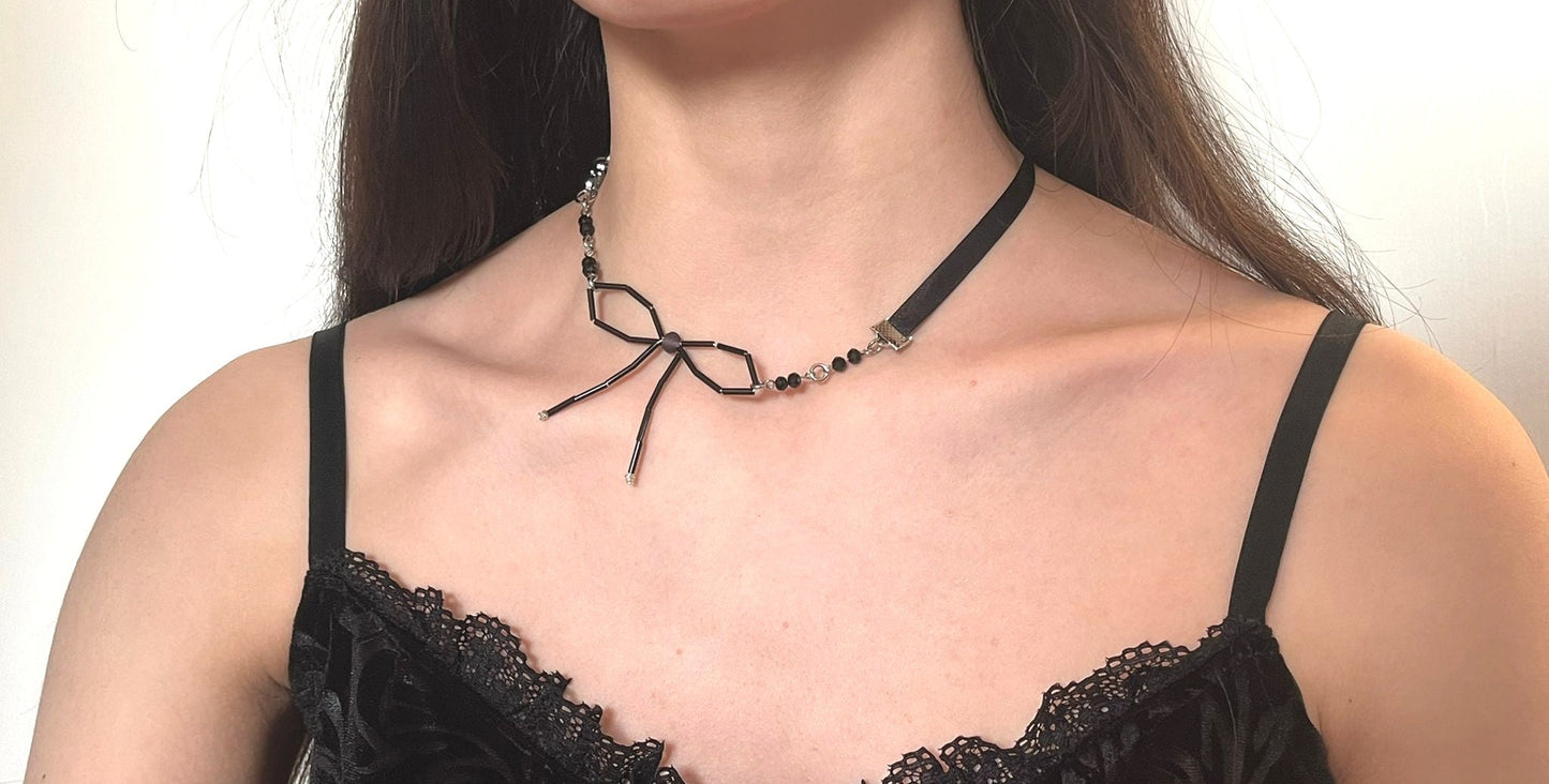 Woman wearing a black lace top and a decorative necklace with a bow on a plain background