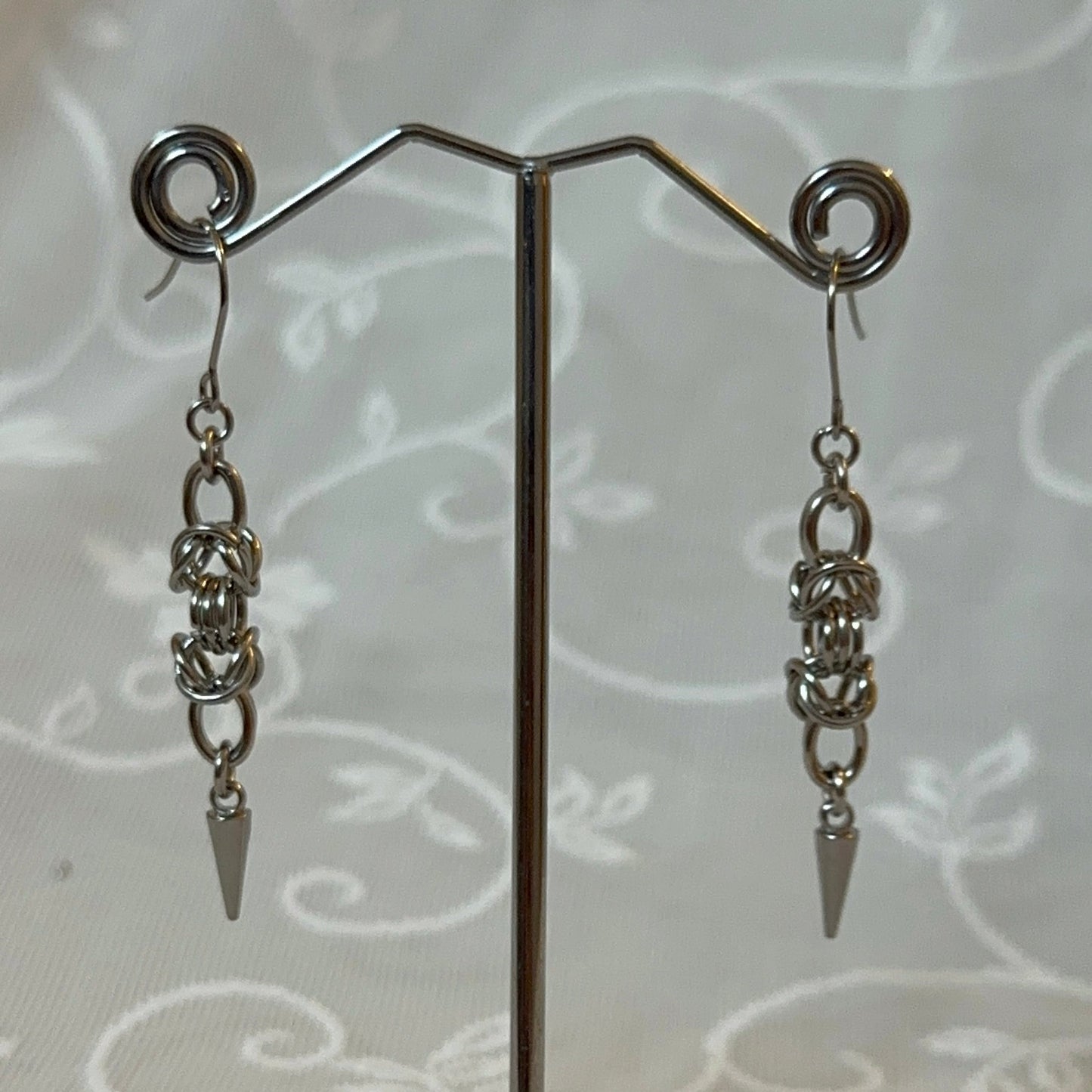 Pair of silver chain earrings on a stand with a white lace background