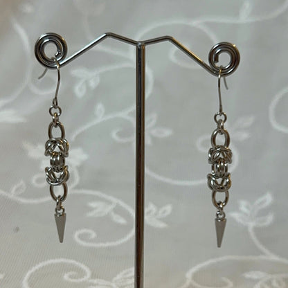 Pair of silver chain earrings on a stand with a white lace background