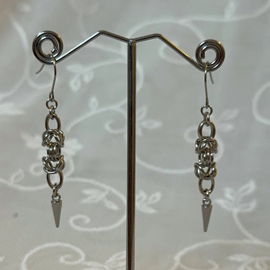 Pair of silver chain earrings on a stand with a white lace background