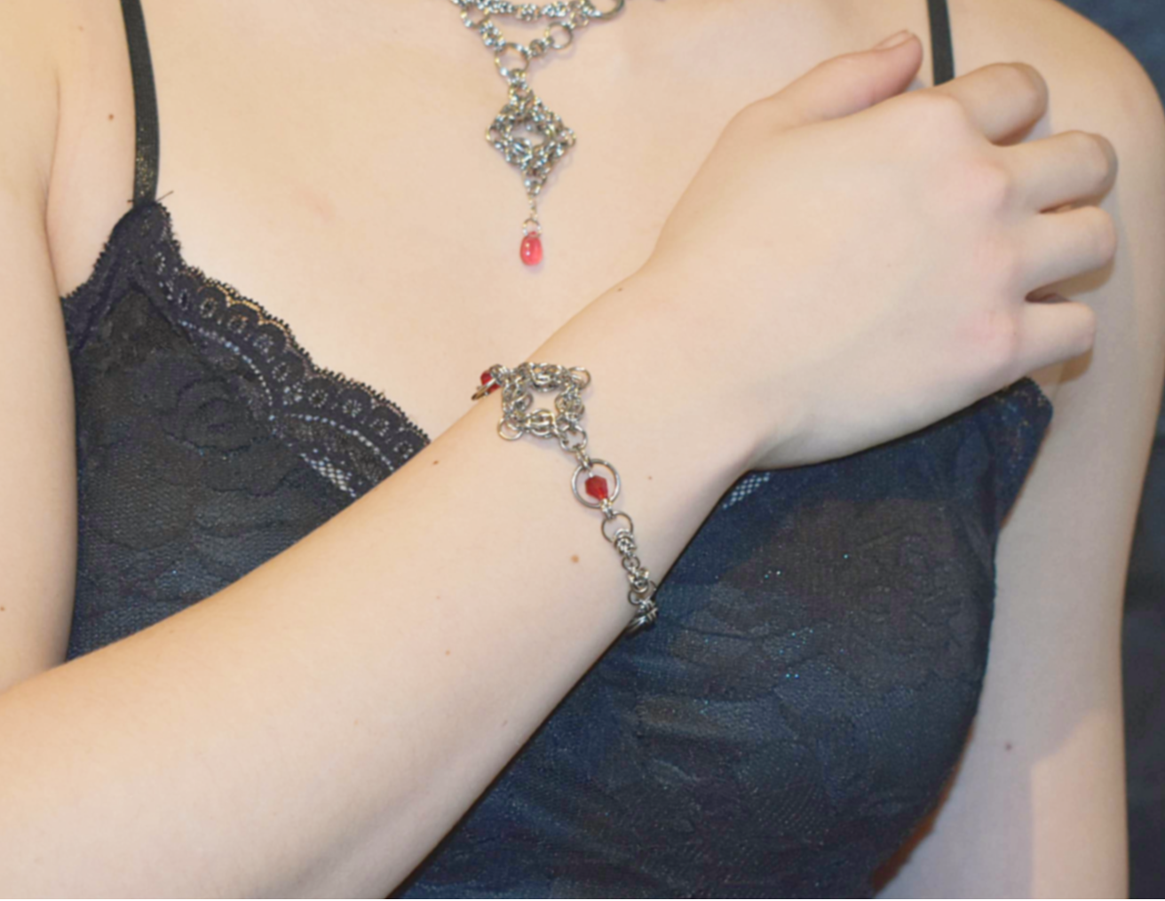 Person wearing a bracelet with a red heart charm, partially visible in a dark top.
