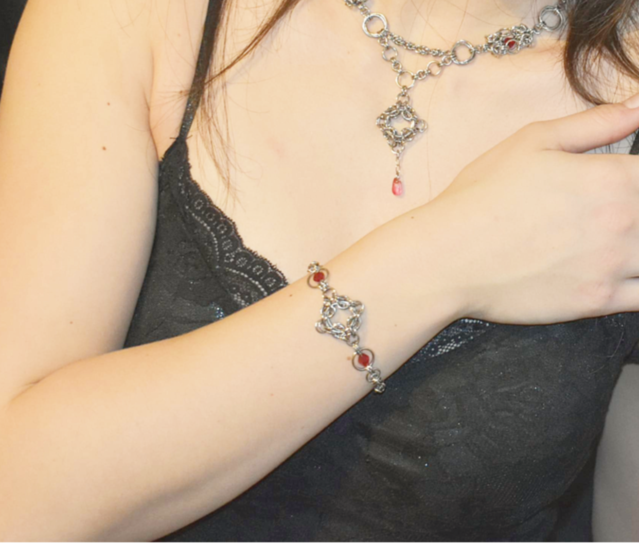 Person wearing a dark gray top and silver bracelet with red stones on a plain background