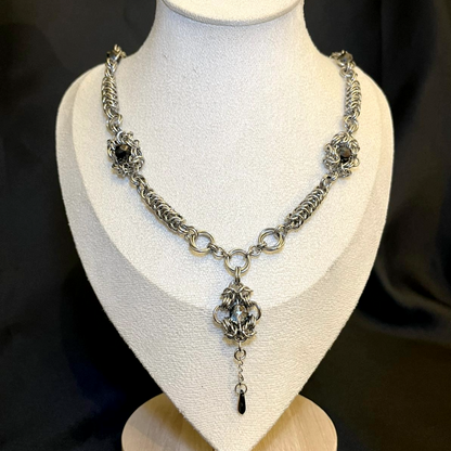 Silver chain necklace with a pendant on a mannequin bust against a dark background