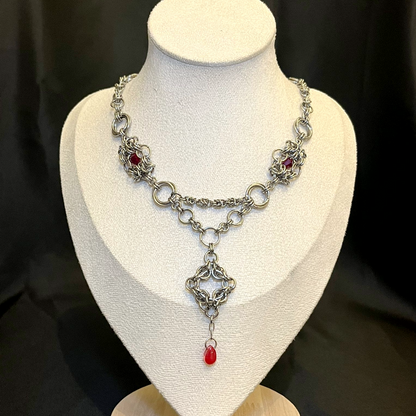 Silver necklace with red accents on a mannequin bust against a black background