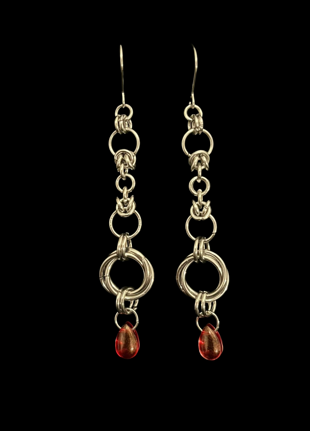 Pair of silver chain earrings with red beads on a black background