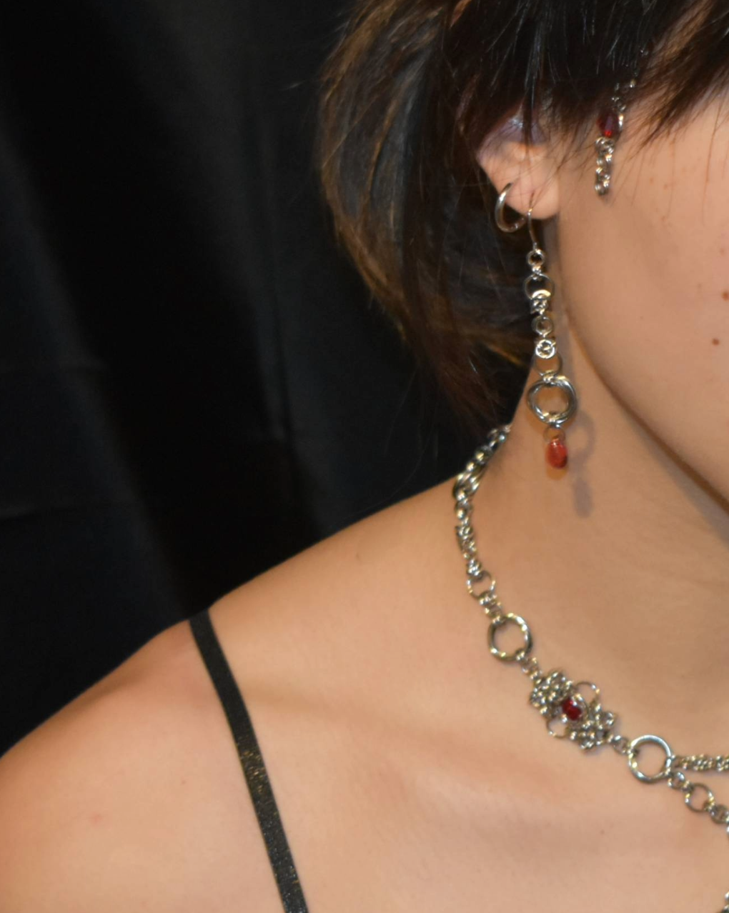 Close-up of a person wearing a silver necklace with red stones and earrings.