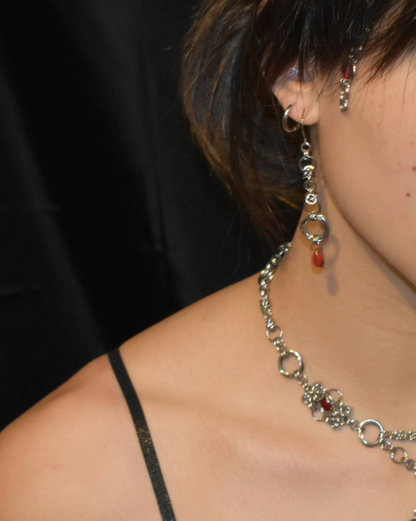 Close-up of a person wearing a silver necklace with red stones and earrings.