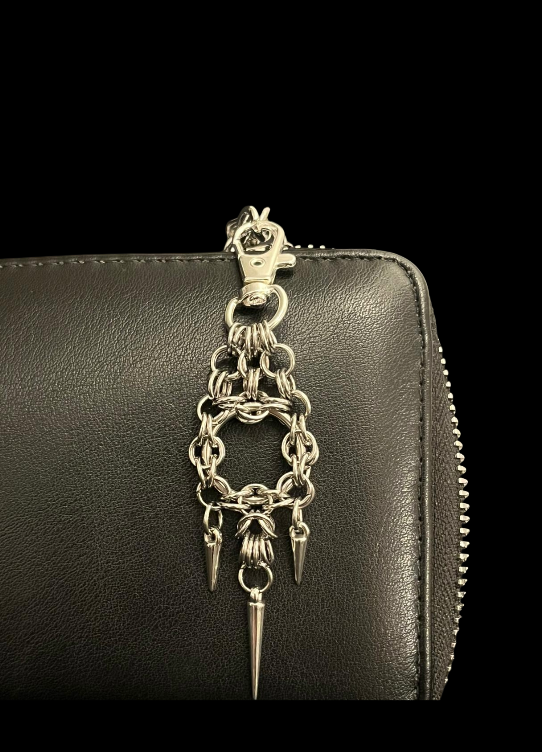 Black leather wallet with a silver chain and spike charm on a black background