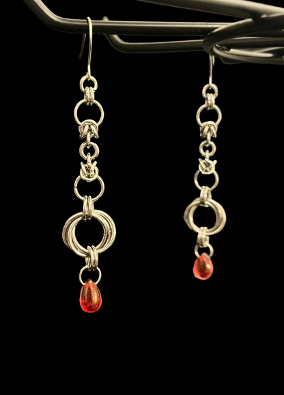 Silver earrings with red drops hanging from a black background