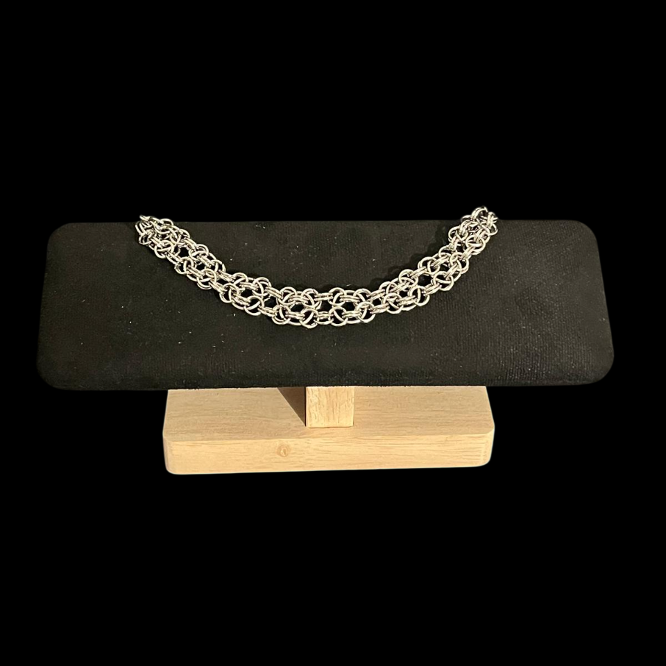 Silver bracelet on a black stone and wooden stand against a black background