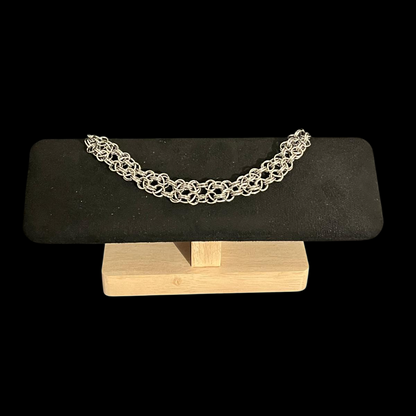 Silver bracelet on a black stone and wooden stand against a black background
