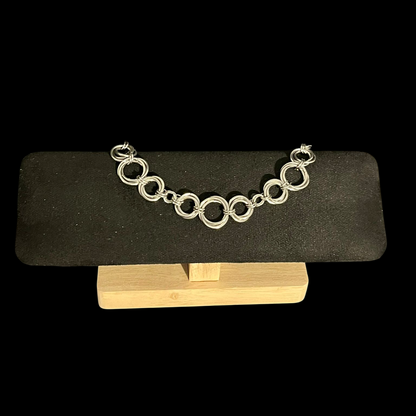Silver chain bracelet on a black stand with a wooden base against a black background