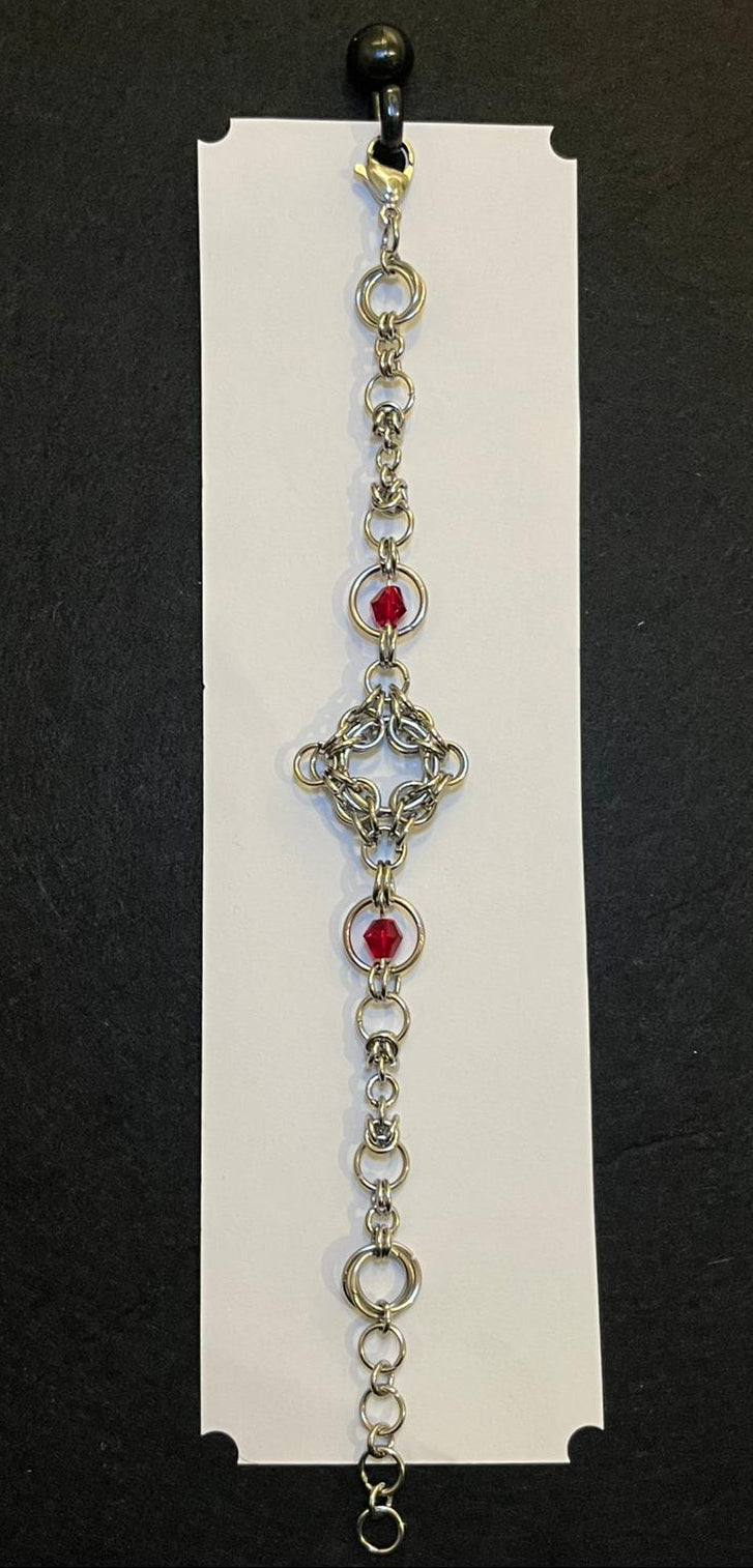 Decorative bracelet with red gemstones on a white card against a black background