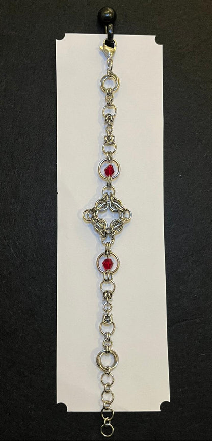 Decorative bracelet with red gemstones on a white card against a black background