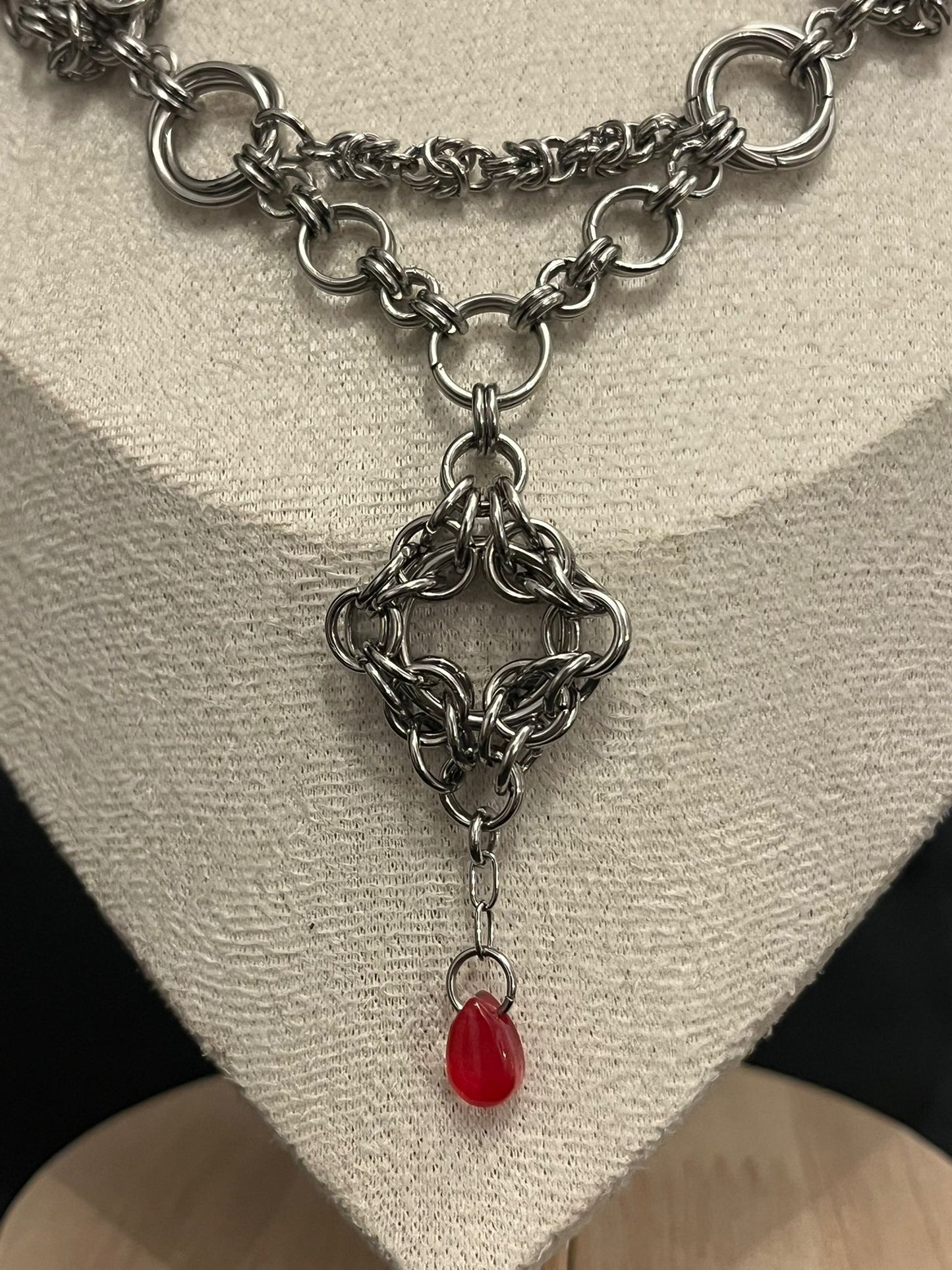 Silver chainmail necklace with a red pendant on a neutral background