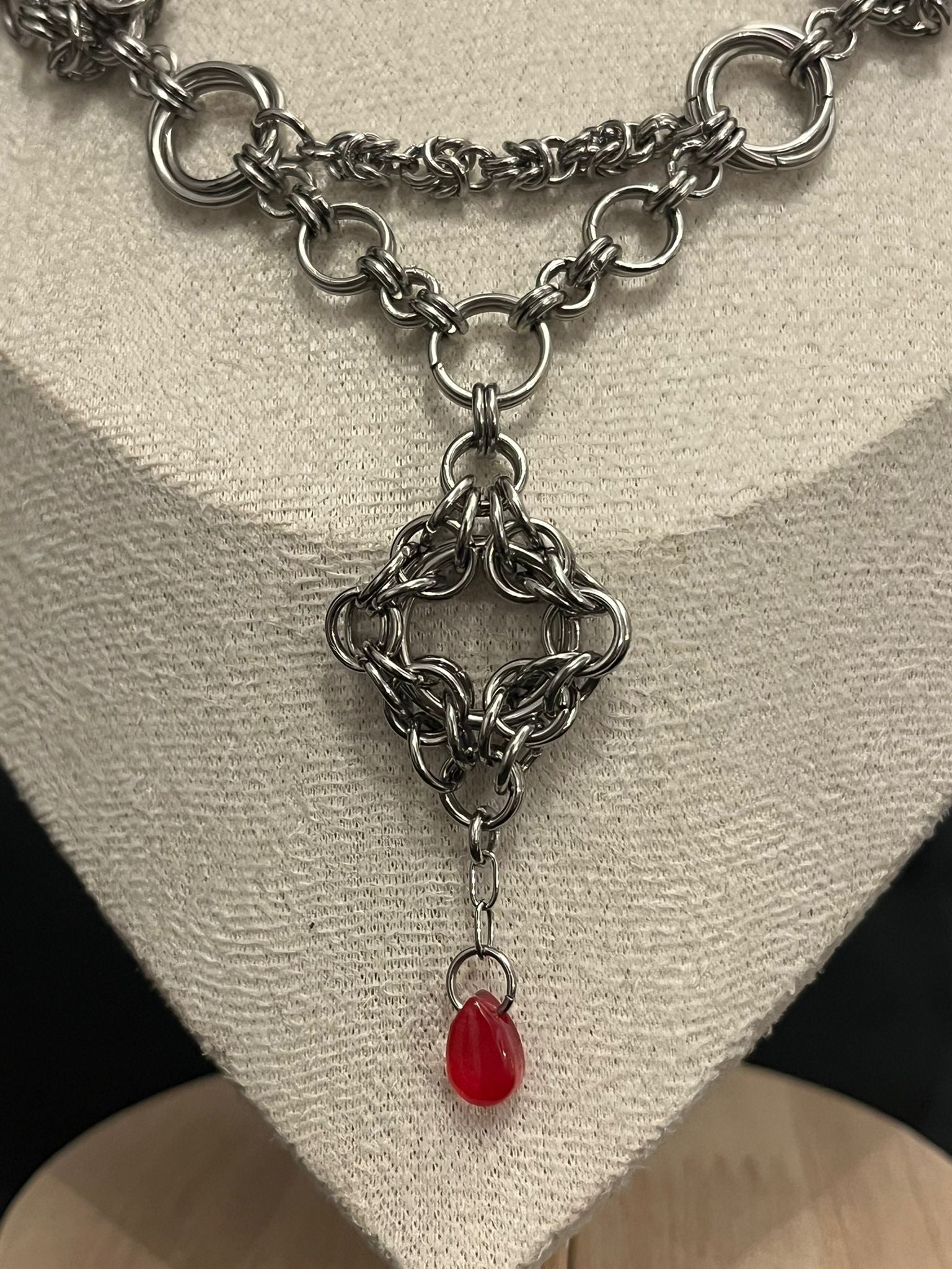 Silver chainmail necklace with a red pendant on a neutral background