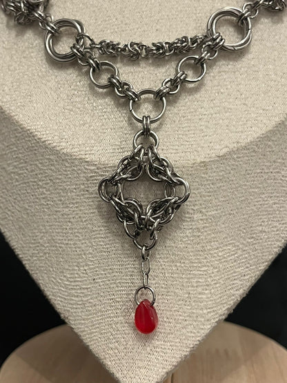 Silver chainmail necklace with a red pendant on a neutral background