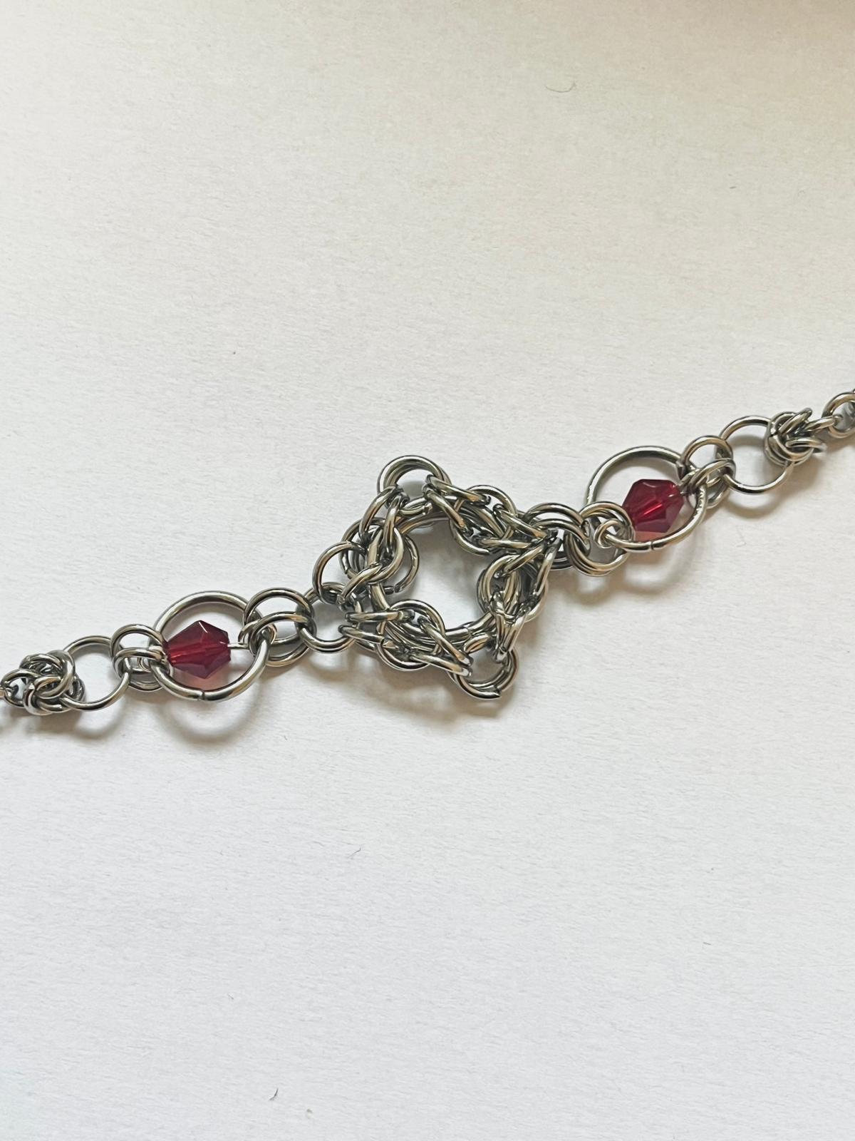 Silver chain bracelet with red beads on a white background