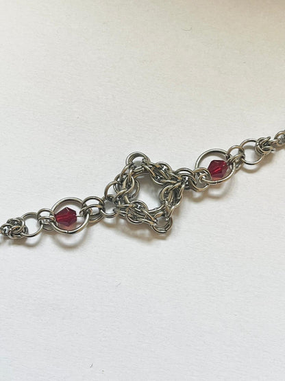 Silver chain bracelet with red beads on a white background