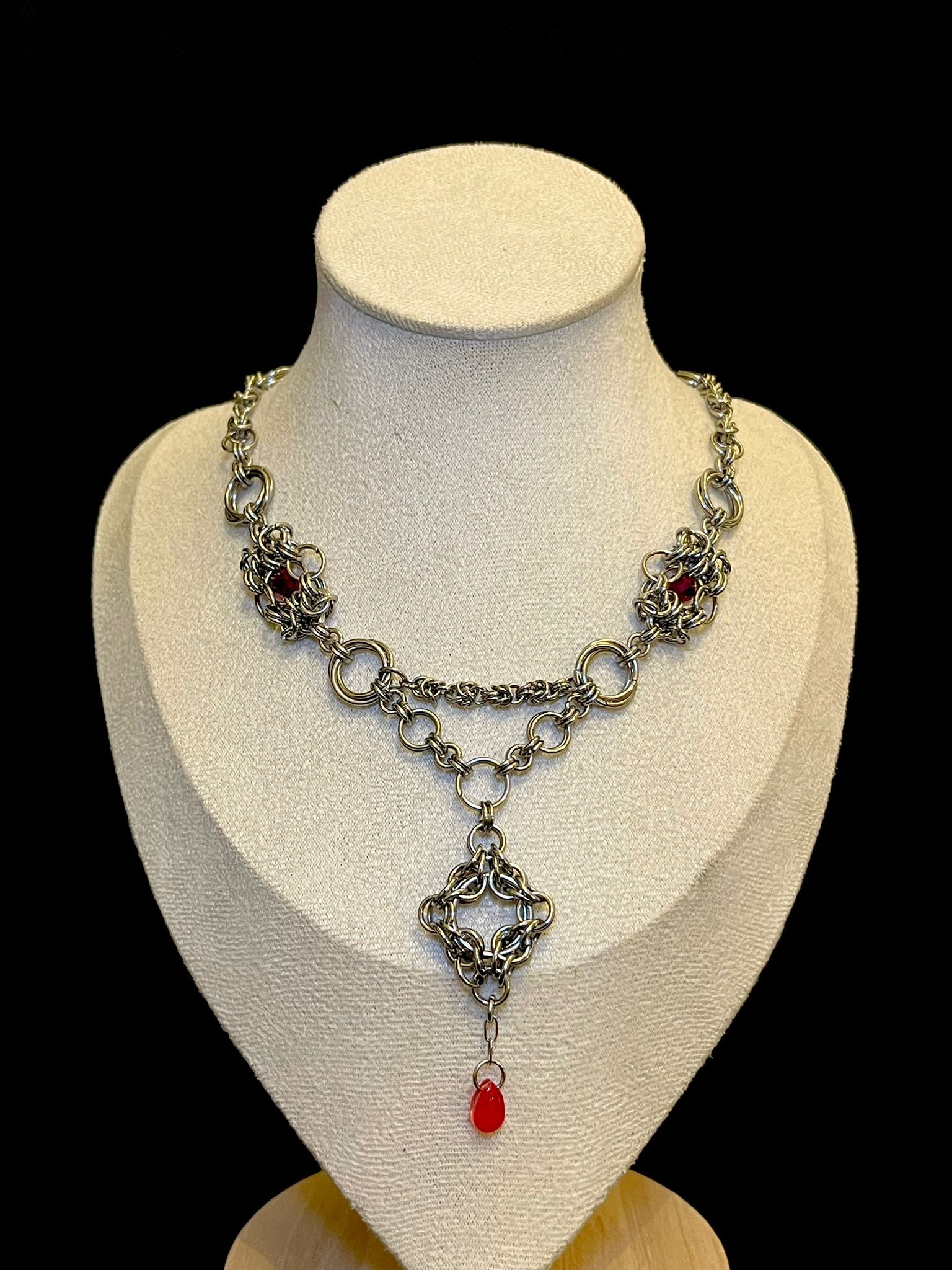 Silver chain necklace with red stones on a mannequin bust against a black background