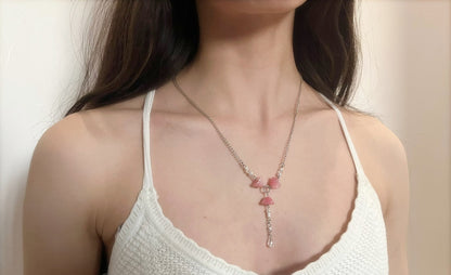 Woman wearing a white tank top with a necklace featuring pink stones against a neutral background