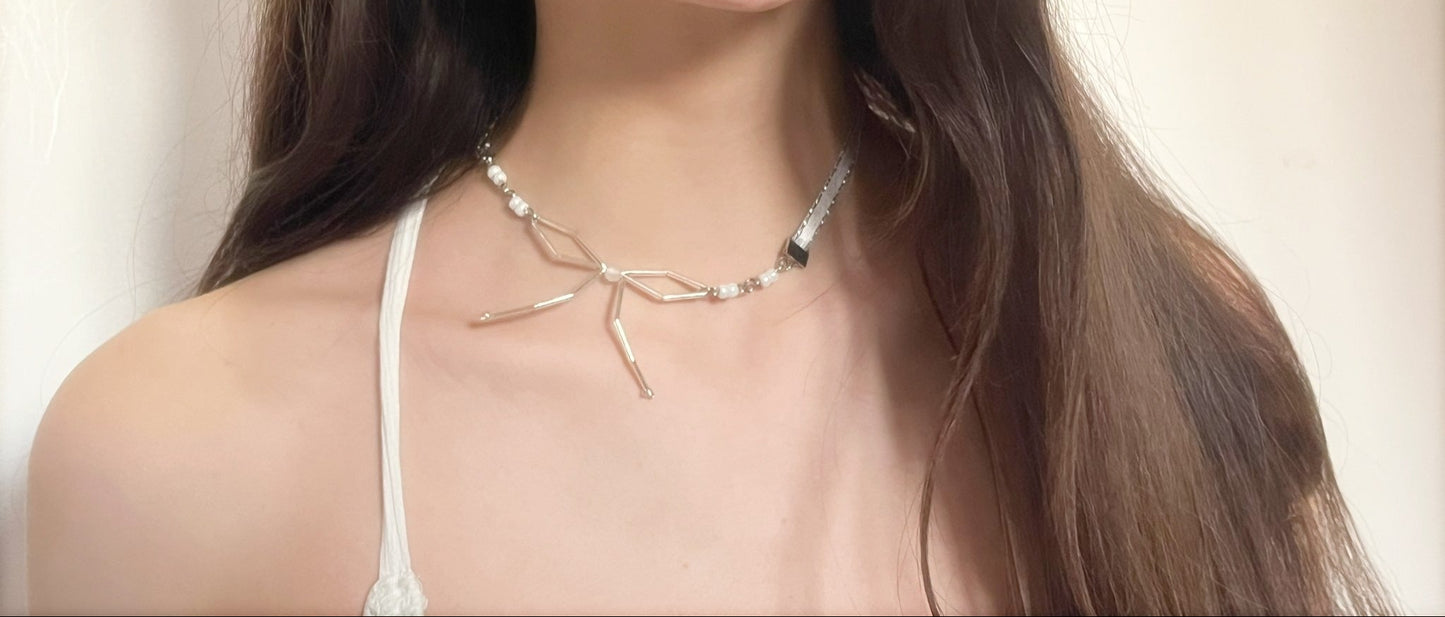 Woman with long brown hair wearing a white tank top and necklace against a plain background