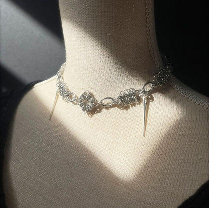 Silver necklace with floral design and spikes on a mannequin bust.