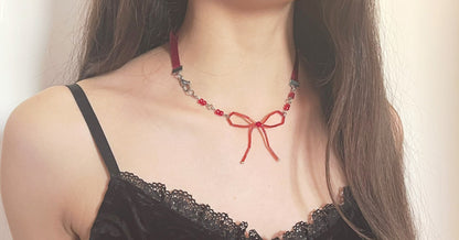 Close-up of a person wearing a black lace top and a red necklace with a bow.