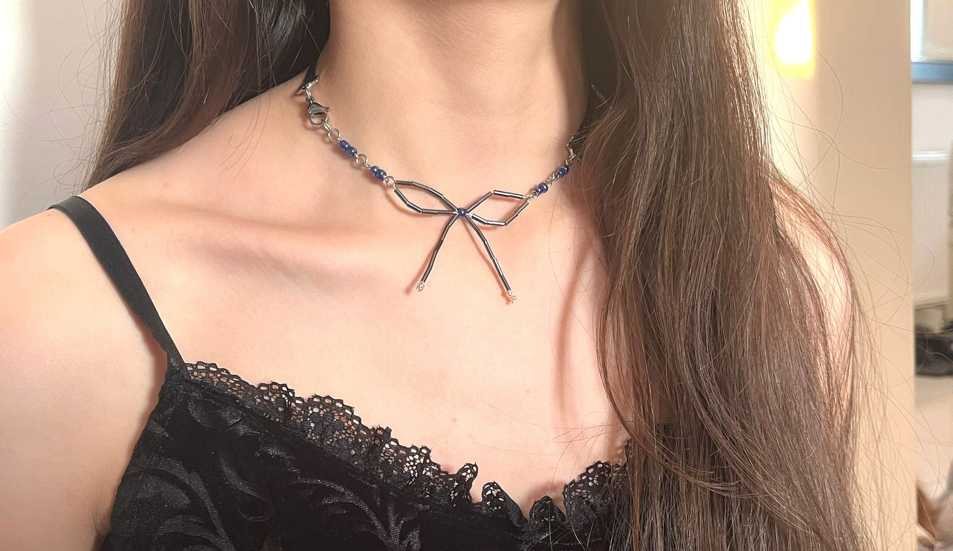 Person wearing a black lace top and a decorative necklace with a bow design.