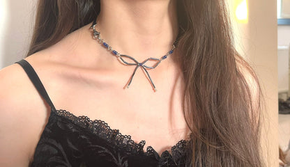 Person wearing a black lace top and a decorative necklace with a bow design.