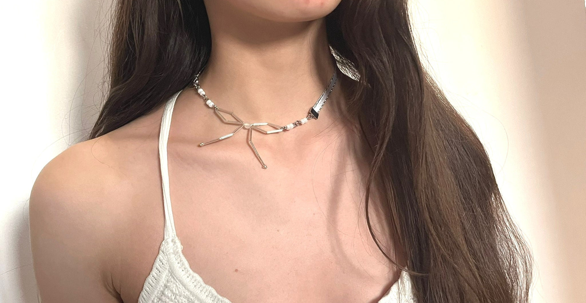 Woman wearing a white top and necklace against a neutral background