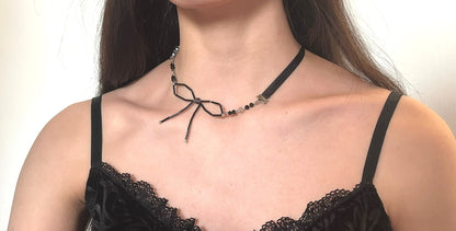 Woman wearing a black lace top and a decorative necklace with a bow on a plain background