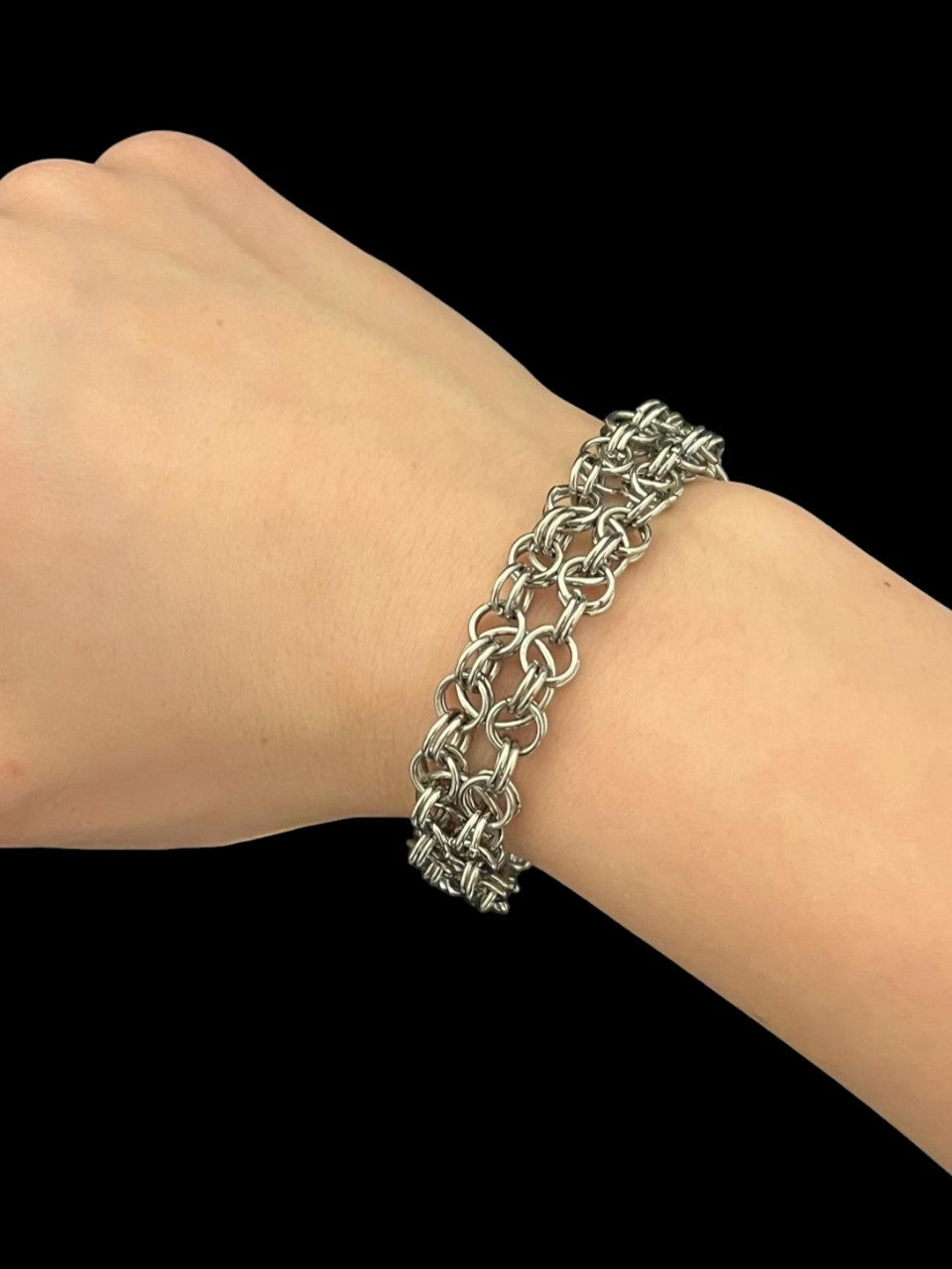 Silver chain bracelet on a wrist against a black background