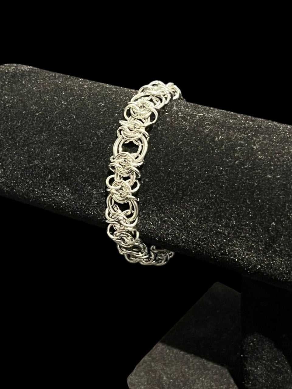 Silver chain bracelet on a black stand with a dark background